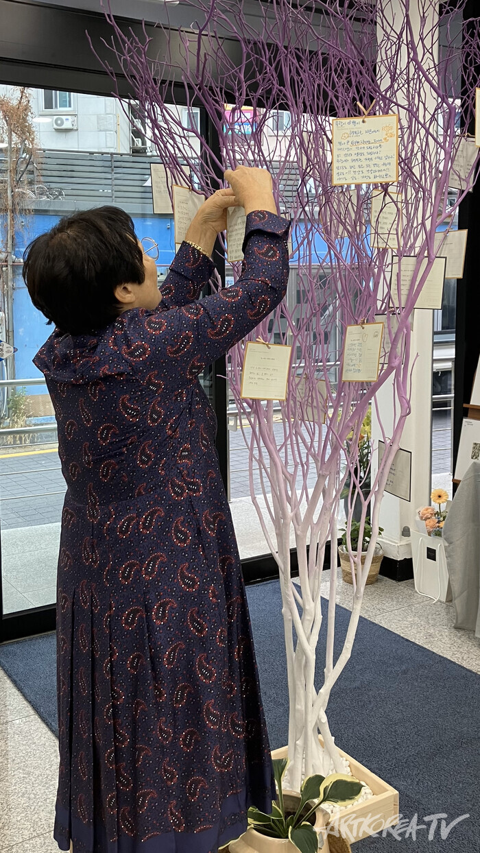 전시 참여자가 '소망의 나무'에 참여자가 쓴 글을 걸고 있다