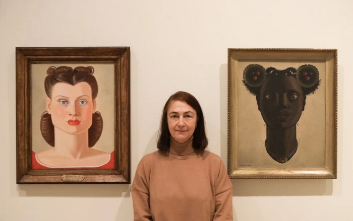 전시의 큐레이터인 파트리샤 몰린스가 2025년 스페인 산탄데르의 센트로 보틴에 설치된 '마루하 말로-가면과 나침반' 전시에 설치된 두 개의 '여성의 머리' 그림 사이에 서 있습니다. 사진-벨렌 데 베니토.